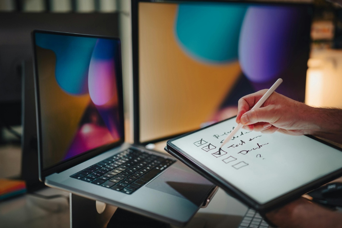 A man sketches on a tablet while focused on his laptop screen, blending digital art and technology seamlessly.