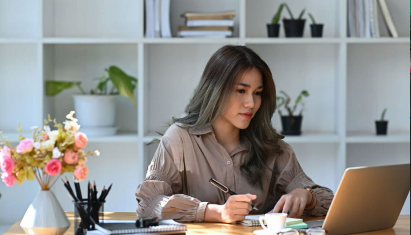 Smart Assistants A Guide for Beginners and the Confused Woman writing notes while using a laptop, representing focus and productivity with smart assistant